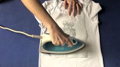 a person ironing a white shirt with a blue iron