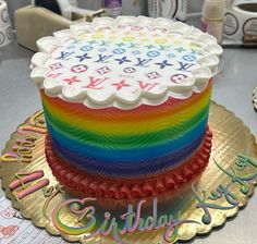 a birthday cake with rainbow frosting and letters on the top is sitting on a gold plate