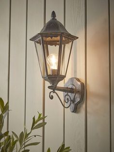 an old fashioned wall light on the side of a building with a potted plant next to it