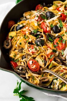 a skillet filled with pasta, olives, tomatoes and parmesan cheese