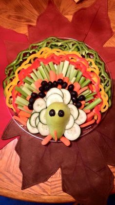 a turkey made out of veggies sitting on top of a wooden table next to a leaf