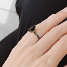 a woman's hand with a black diamond ring on her finger and gold band