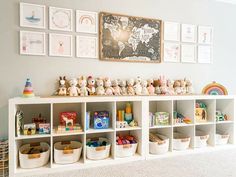 a white shelf filled with lots of toys next to a wall covered in framed pictures