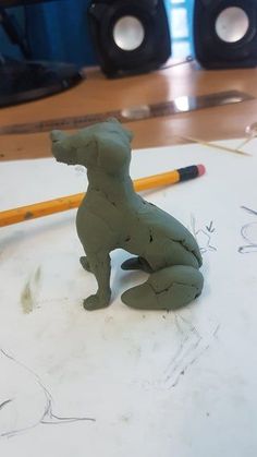 a clay dog sitting on top of a table next to a pencil