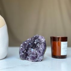 a purple rock next to a candle on a white counter top with a vase in the background