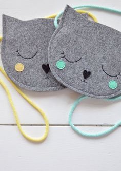 two gray cat face masks with green eyes and ears on top of each other next to a yellow string