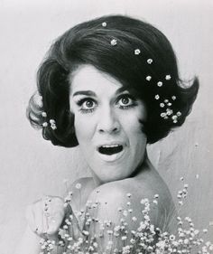 a black and white photo of a woman with flowers in her hair looking surprised at the camera