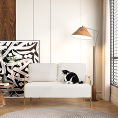 a black and white cat sitting on a white couch in front of a large painting