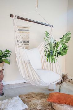 a white hammock hanging from the ceiling in a room with plants and rugs