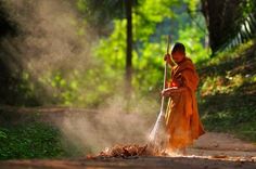 a woman in an orange robe is sweeping up dirt from the ground with a broom