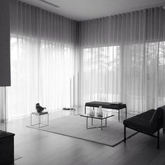 a black and white photo of a living room with sheer curtains on the window sill