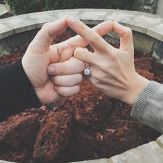 two hands holding each other's fingers in front of a brick planter with dirt on the ground