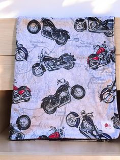 a blanket with motorcycles printed on it sitting on a wooden bench next to a wall