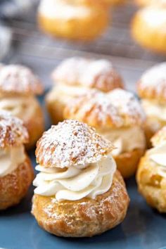 small pastries with icing and powdered sugar sitting on a blue plate in front of other pastries