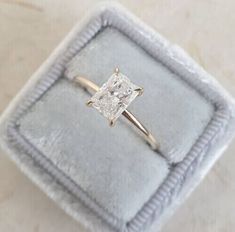 an engagement ring with a princess cut diamond in it on a velvet box that is sitting on a table