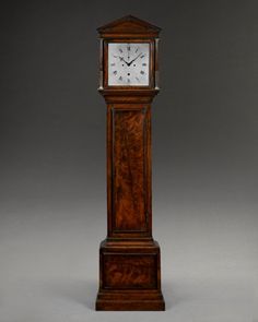 a tall wooden clock with roman numerals on the face and sides, standing in front of a gray background