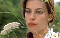 a woman with blue eyes standing next to some wildflowers and looking at the camera