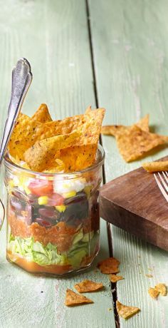 a jar filled with salad and chips on top of a wooden table