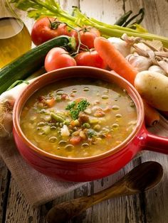 a red bowl filled with soup sitting on top of a table next to bread and vegetables