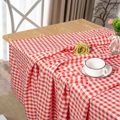 a red and white checkered table cloth with a cup, saucer and flower