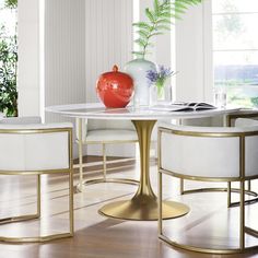 a dining room table with white chairs and a red vase sitting on top of it