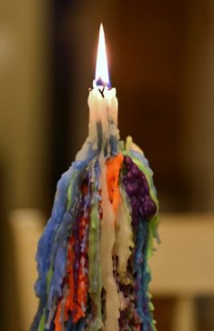 a multicolored cake with a lit candle sticking out of it's center