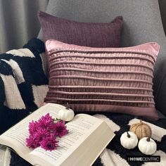 an open book and some flowers on a chair with a striped throw pillow behind it