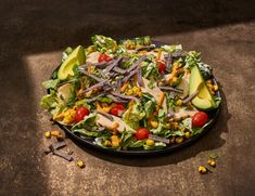 a salad with avocado, corn, tomatoes and other vegetables on a black plate