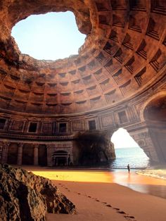 a person walking on the beach in front of an arch shaped structure that looks like it has been built into the ground