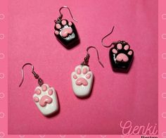 three pairs of earrings with pink and black paw prints on them, one is dangling from the