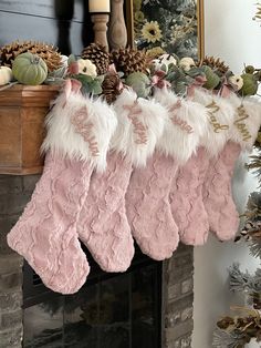 three pink stockings hanging from a mantel decorated with pine cones, flowers and greenery