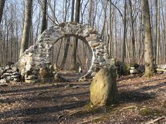 a stone arch in the middle of a wooded area with trees and rocks around it