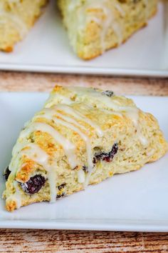 two white plates topped with scones covered in icing and cranberry toppings