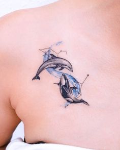 two dolphins tattoo on the back of a woman's shoulder