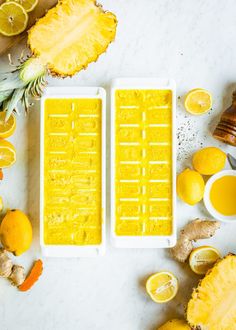 two ice trays filled with yellow liquid next to sliced oranges and pineapples