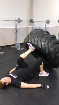 a woman laying on the ground with a large tire in front of her and another person standing next to it