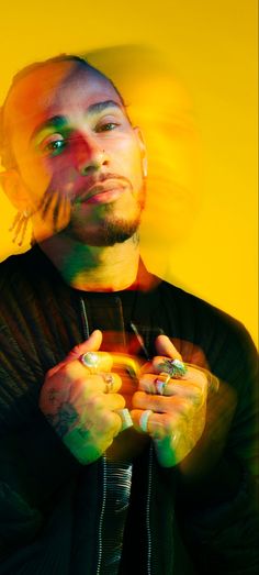 a man with tattoos and piercings holding his hands together in front of a yellow background