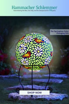 a colorful lamp sitting on top of a metal stand in the grass with flowers painted on it