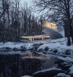 the house is surrounded by snow covered trees and rocks, with water running through it