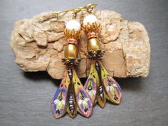 These earrings use enameled copper charms by 2Moiselles in France. The winged charms are decorated with a gorgeous butterfly motif in indigo, yellow and white with black accents.  Above the charms navy enamel and rhinestone enamel bead caps followed by copper cone shaped bead caps.  Pink rhinestone spacers set in gold come next.  Shimmering freshwater pearls nested inside a double layer of pronged copper bead caps sit atop the rhinestone spacers.  Scalloped gold  bead caps top off these unique b Bohemian Gold Enamel Earrings, Whimsical Hand Painted Gold Earrings, Bohemian Gold Hand Painted Earrings, Bohemian Hand Painted Gold Earrings, White With Black Accents, Butterfly Motif, Earrings Colorful, Enamel Beads, Enameled Copper