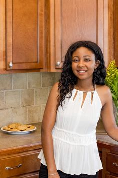 a woman standing in front of a counter with cookies on it and flowers behind her