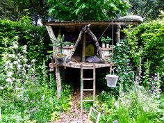 a tree house made out of branches in the middle of some plants and flowers around it