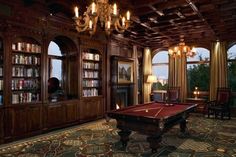 a pool table is in the middle of a room with many bookshelves and chandeliers