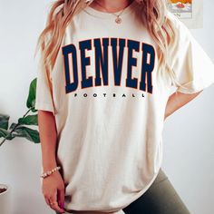 a woman wearing a denver football t - shirt standing next to a potted plant