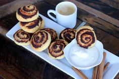 cinnamon buns on a white plate next to a cup of coffee and cinnamon sticks