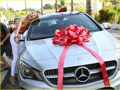 a woman standing next to a silver car with a red bow on it