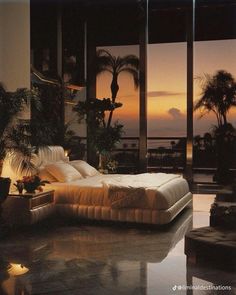 a large bed sitting in the middle of a bedroom next to tall windows with palm trees