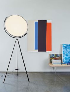 a floor lamp sitting next to a table with pictures on it and a painting on the wall