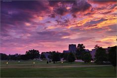 the sky is purple and pink as it sets over a grassy field in front of a large building