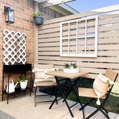 two chairs and a table on a wooden deck near a brick wall with a window